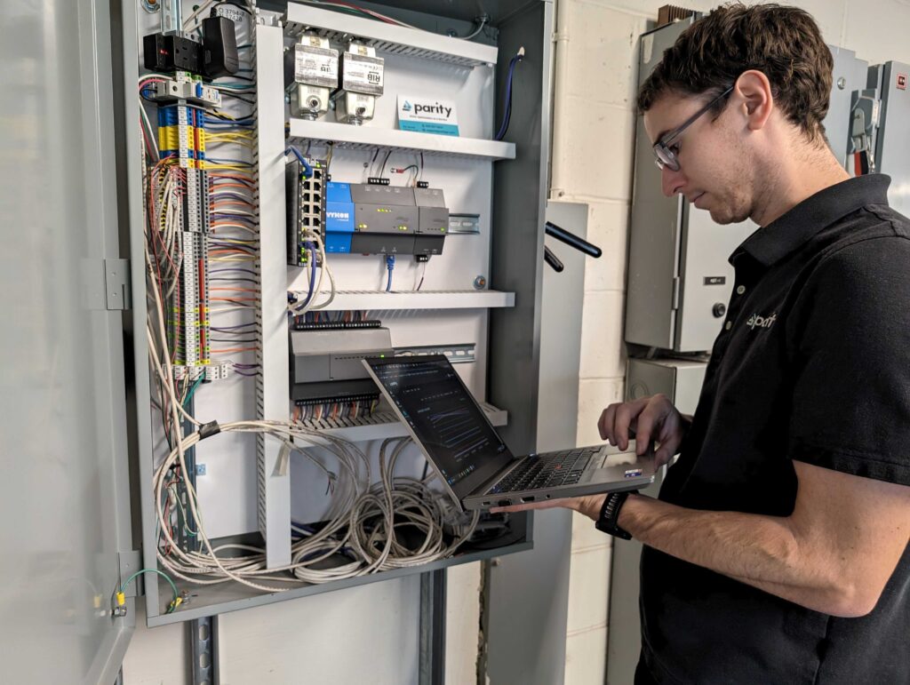 Stuart looking at Pi while standing in front of a control panel and other HVAC systems in a Parity operated building.