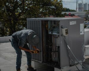 Image of a man repairing an HVAC system on the rooftop because it's an Inefficient HVAC Systems.